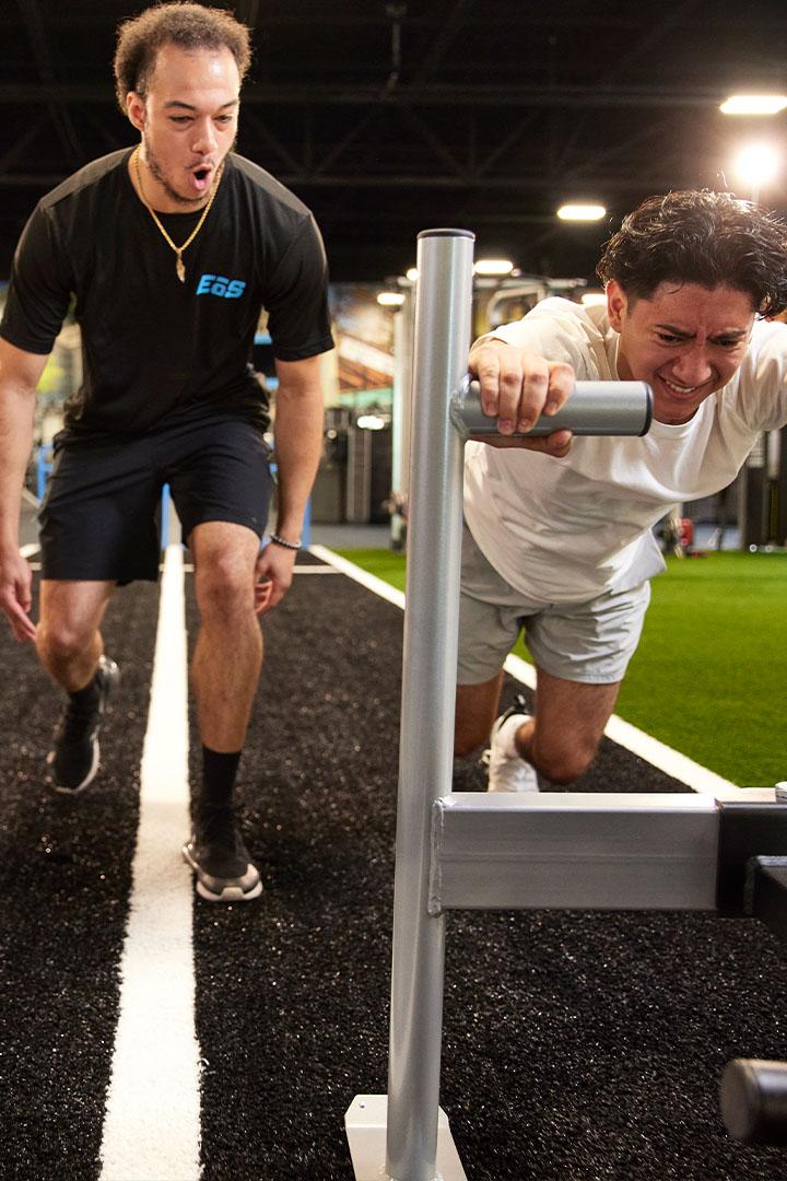 Trainer encouraging a man pushing a sled on a gym turf