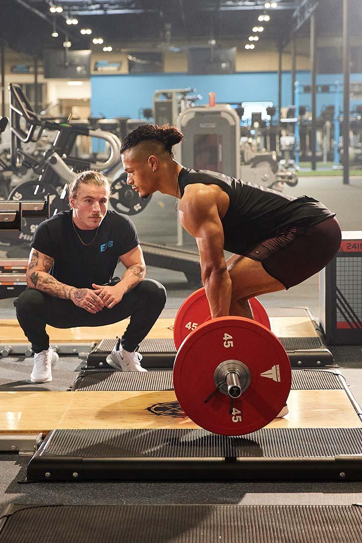 Trainer supervising a man performing a deadlift in a gym