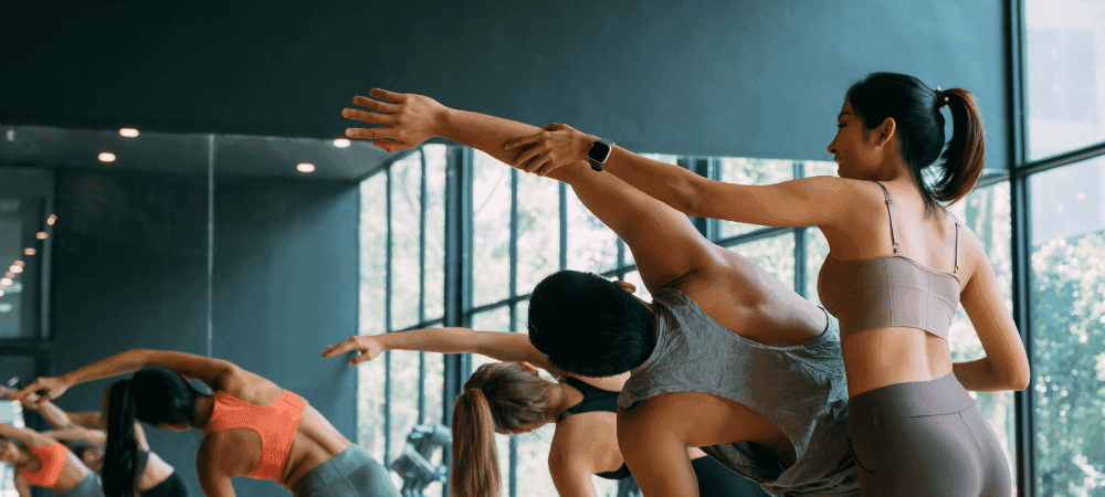 group of athletic eos gym members helping each other in a deep stretch in a well lit yoga studio