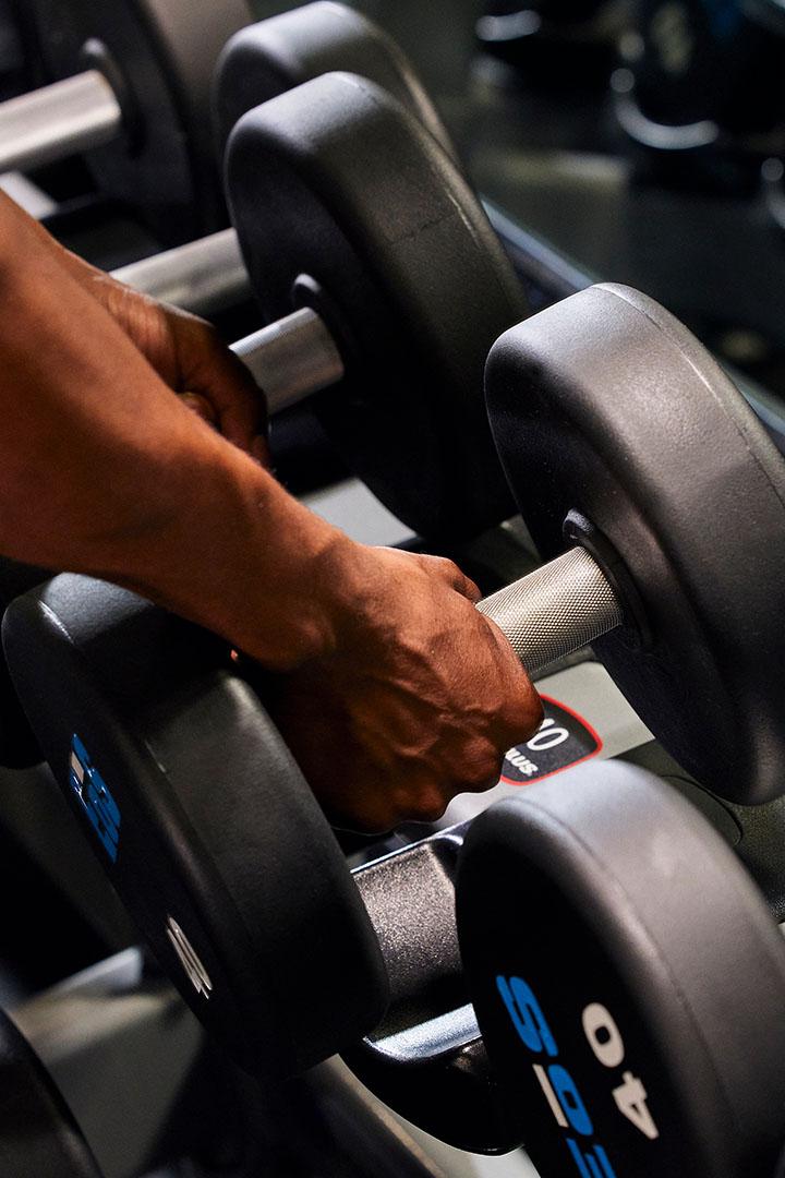 Hands picking up a dumbbell from a rack in the gym