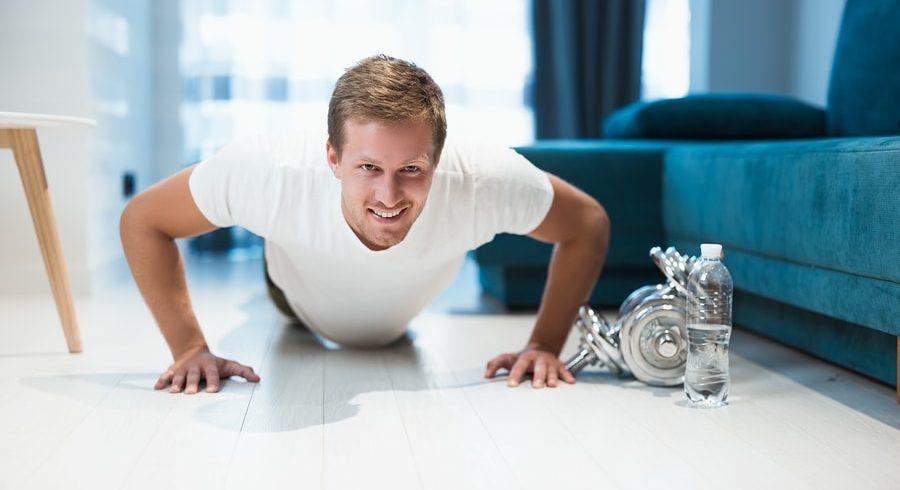 Man doing push-ups at home next to dumbbells and a water bottle