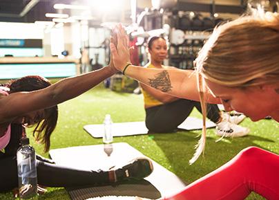 two eos gym members stretching in indoor turf while high fiving