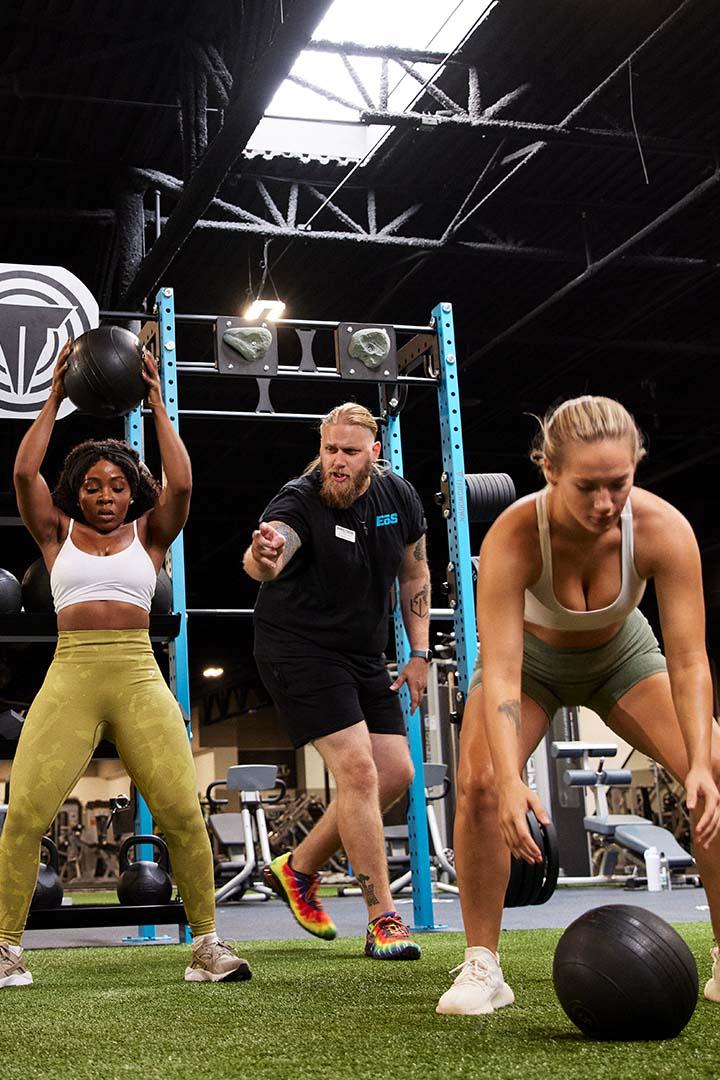 Trainer coaching two women during a workout with medicine balls