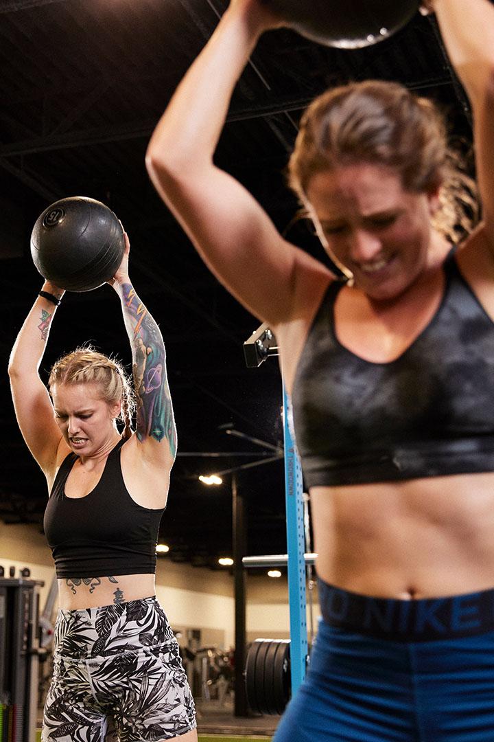 Two women lifting medicine balls overhead during a workout