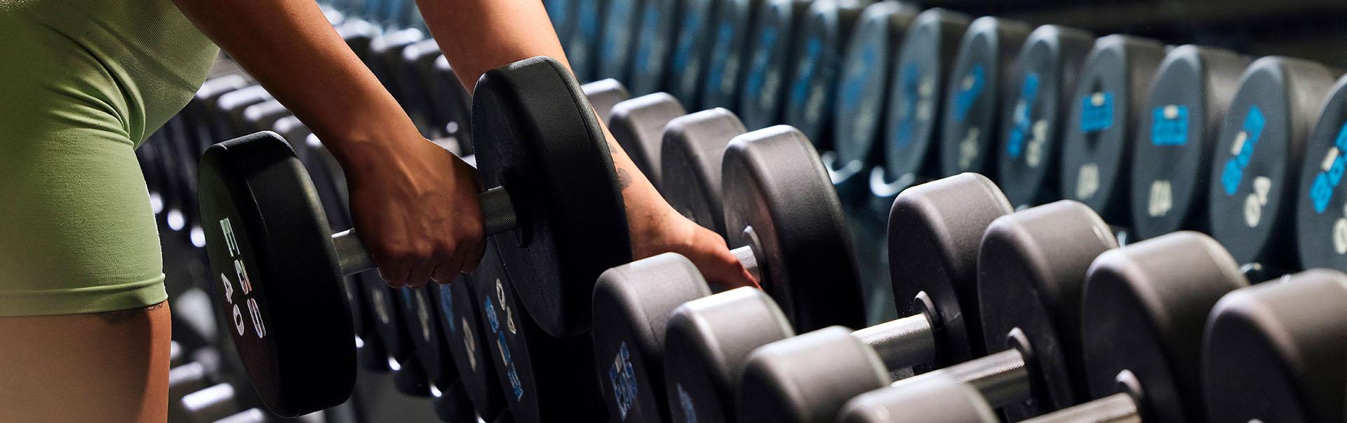 close up shot of eos gym member unracking a dumbbell from a large eos branded rack of weights