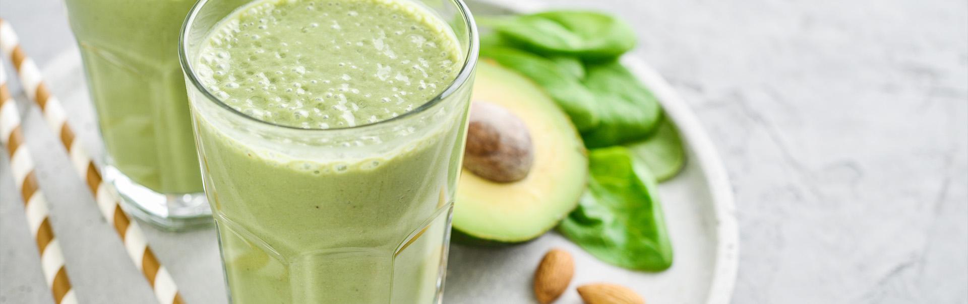 two full glasses of green smoothies accompanied by nuts and fresh avocado 