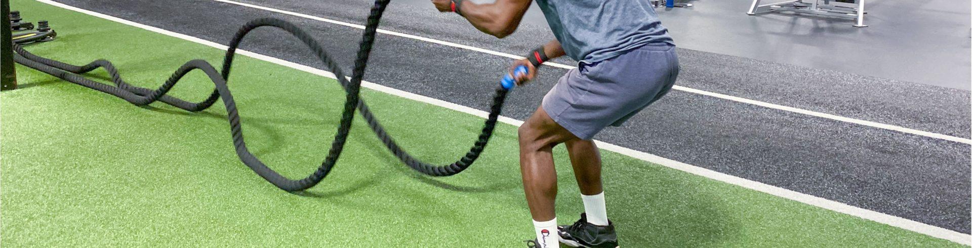 eos gym member working out with with battle ropes on turf