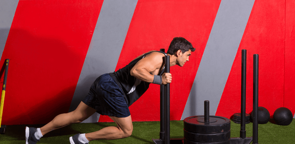 eos gym member pushing a sled on indoor turf