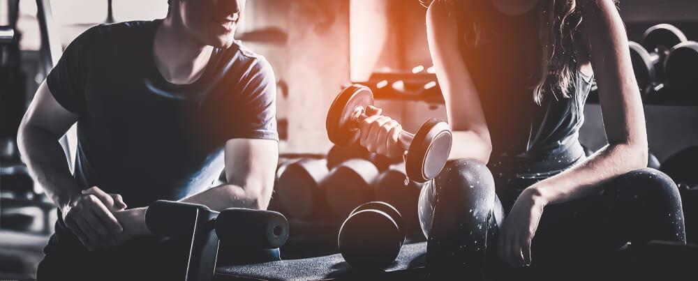 Crop image of beautiful sport girl with dumbbell in hand with personal trainer in professional gym