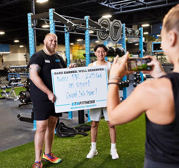 eos gym member and personal trainer getting their photo taken holding up how much weight they lifted