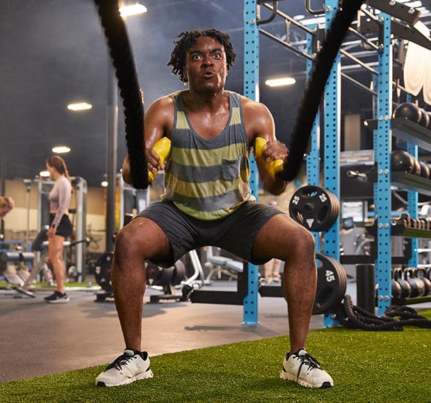 eos gym member in tank top working out with the battle ropes on indoor turf