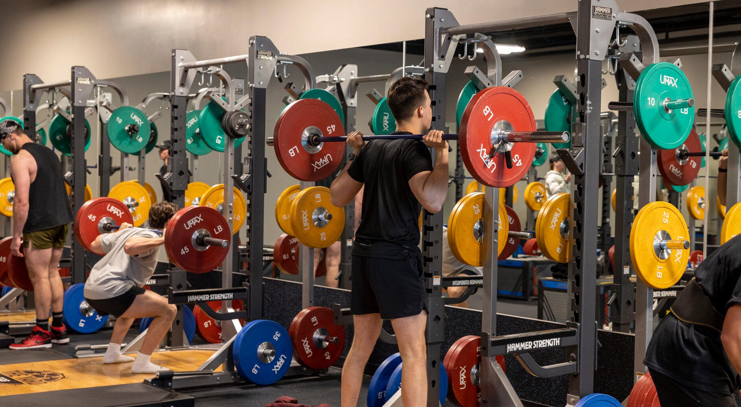 eos gym member barbell squatting in a fully equipped squat rack